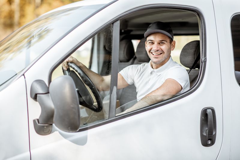 Smiling delivery driver sitting in a van, representing friendly and reliable courier service.