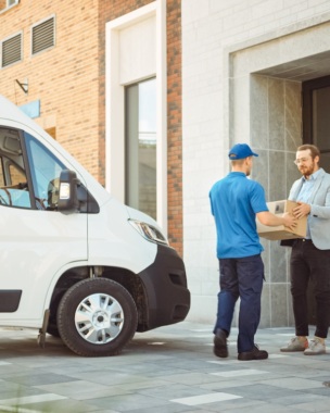 Delivery Man Gives Postal Package to a Business Customer, Who Signs Electronic Signature POD Device. In Stylish Modern Urban Office Area Courier Delivers Cardboard Box Parcel to a Man.