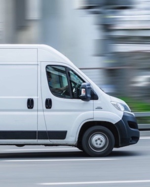 White Fiat Ducato cargo van with tall roof is driving on the street, side view. Light commercial vehicle in motion