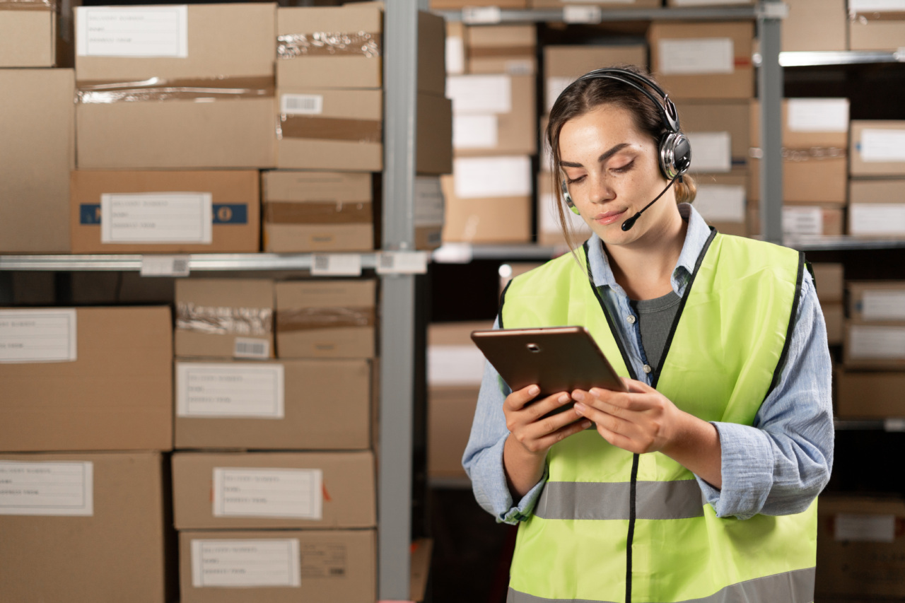 Female worker wearing headsets in logistics warehouse working with inventory app using digital tablet.