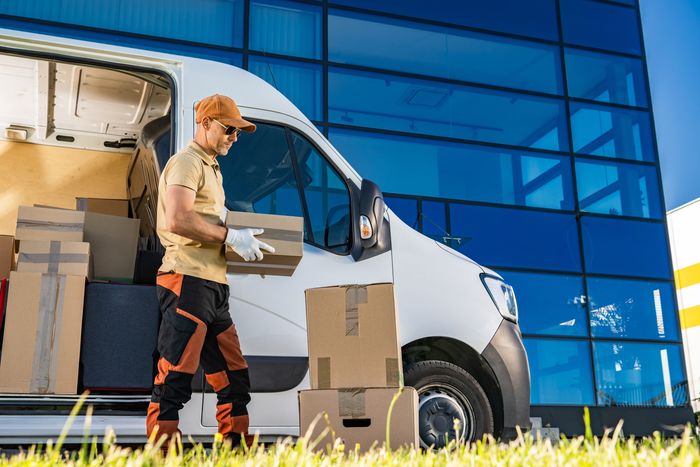 Courier loading boxes into van in front of building.
